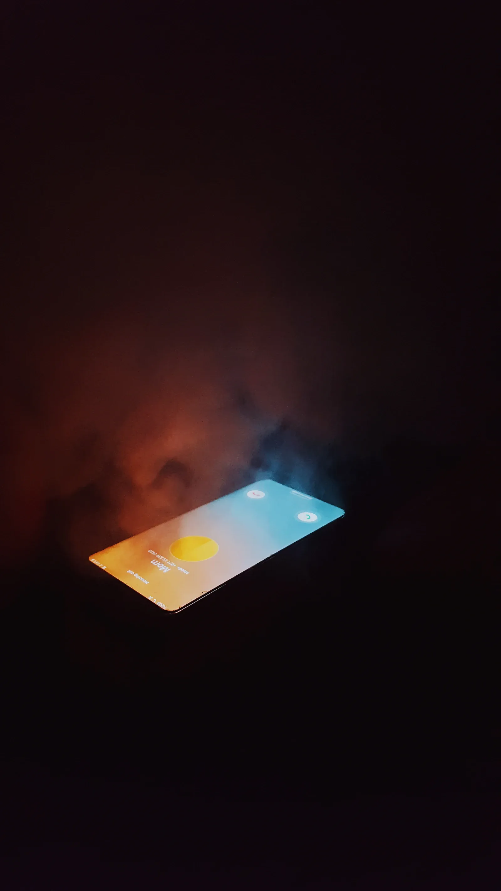 Celular con la pantalla encendida sobre un fondo oscuro, rodeado de humo de colores