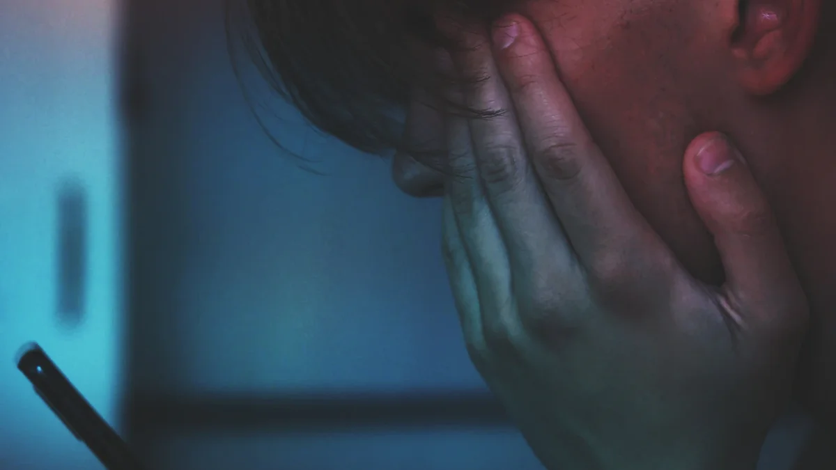 Persona con la cara apoyada en la mano y un celular en la otra mano